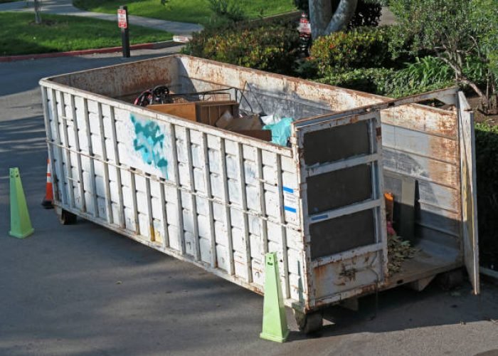 a white dumpster with one door open and lots of trash and furniture inside.